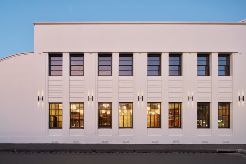 Street facade with vertical pilasters, tall windows, and horizontal louvers under a blue sky