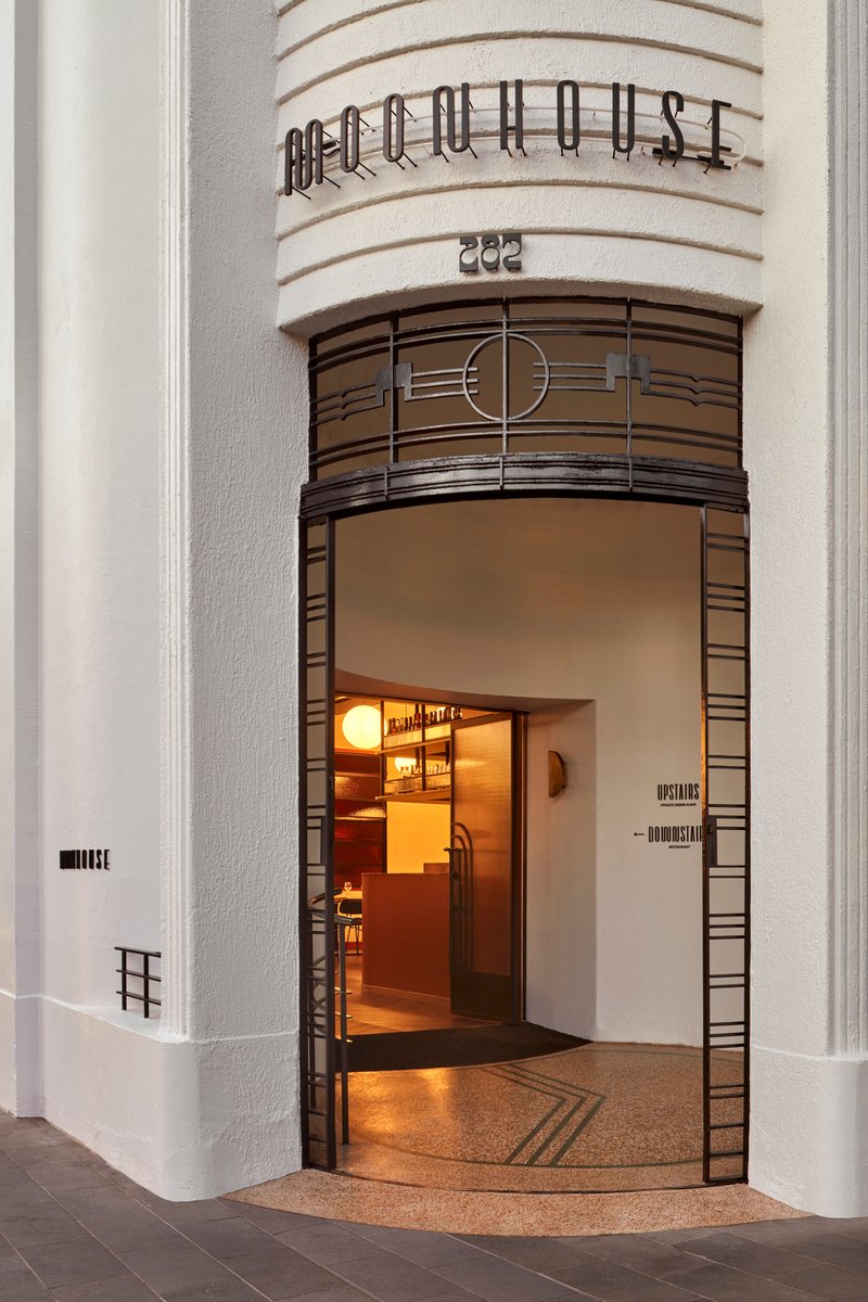 Corner entrance with metal grille surround, curved lettering above, and terrazzo threshold at twilight