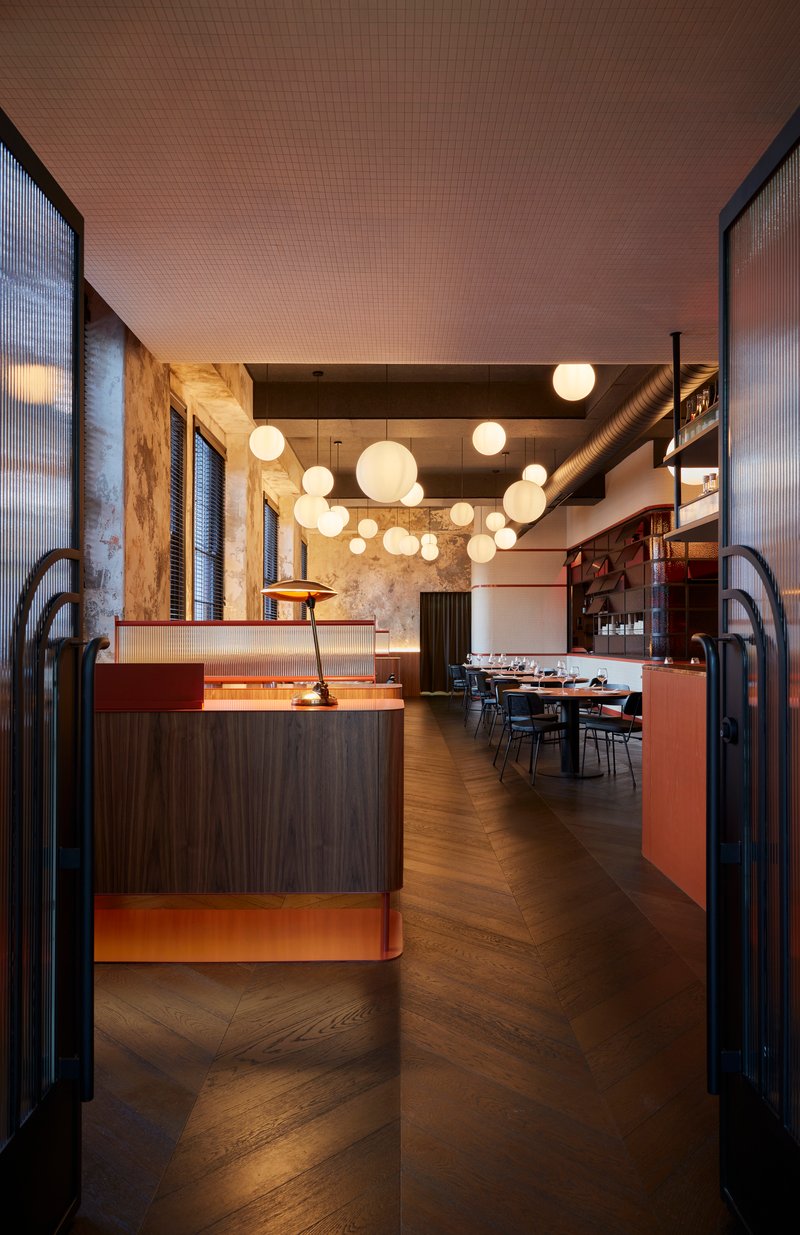 Interior view through arched steel entry doors showing reception desk with globe pendants and herringbone flooring