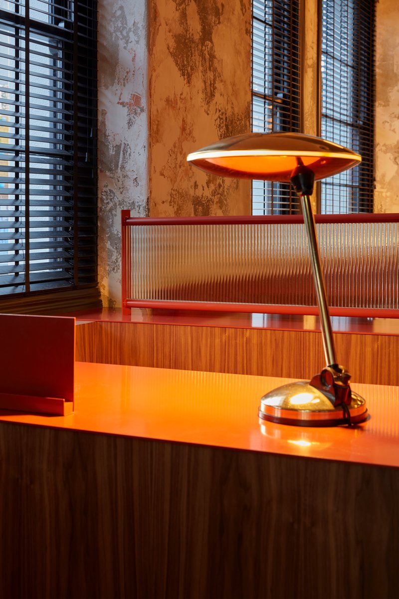 Close-up of brass desk lamp on orange counter with ribbed glass panel and weathered plaster wall