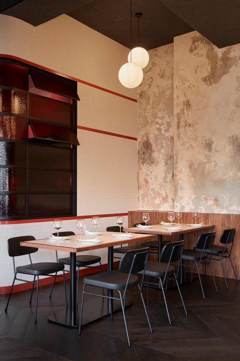 Dining tables against weathered plaster walls with dark wood shelving and white mosaic tile wainscoting