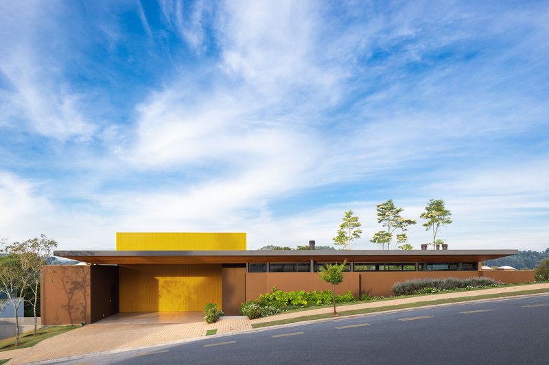 Street view of the low-slung roofline with yellow perforated screen and terracotta walls under scattered clouds