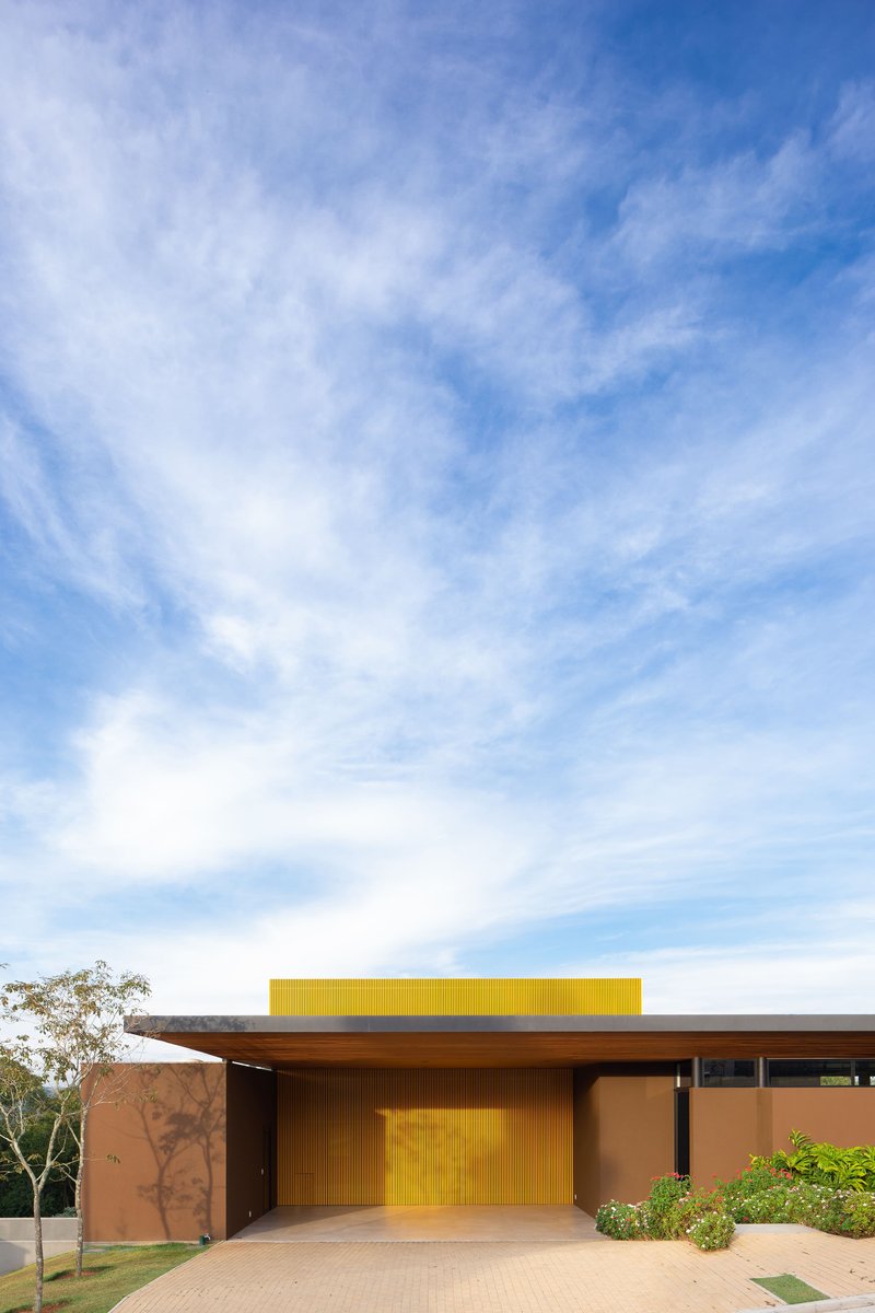 Entry facade with yellow portal and horizontal roof plane under wispy clouds