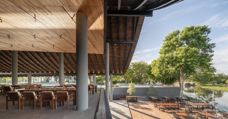 Dining terrace with timber columns and exposed roof beams overlooking waterfront deck and mature trees