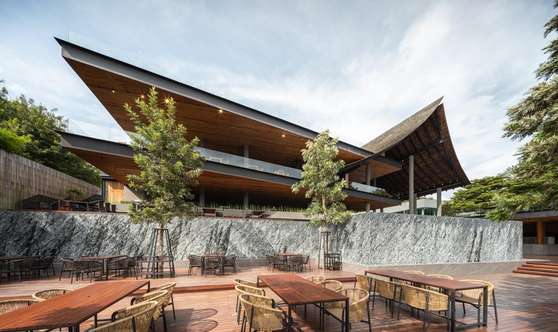 Outdoor terrace with timber decking and wicker seating below cantilevered roofs and a textured stone wall