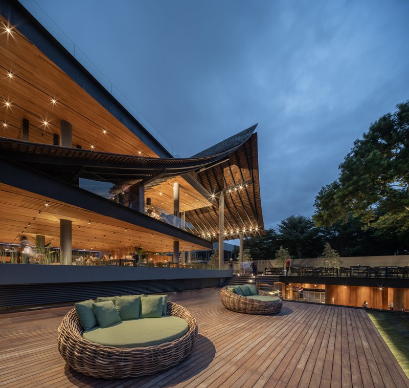 Wooden deck terrace with woven loungers beneath the sculptural roof at blue hour