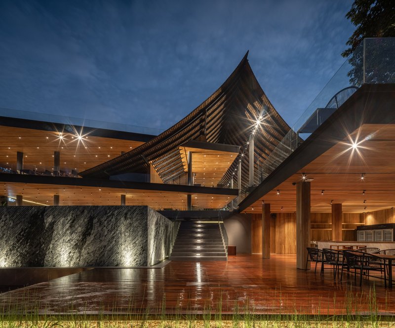 Night view of the illuminated stone wall and reflective pool beneath the tilted roof