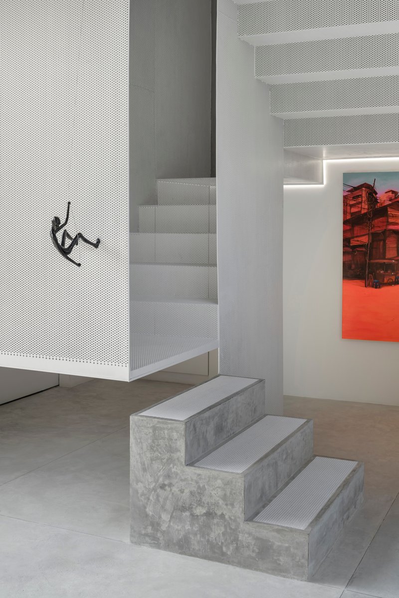 White perforated metal staircase ascending past a concrete stepped base and a red artwork in the background