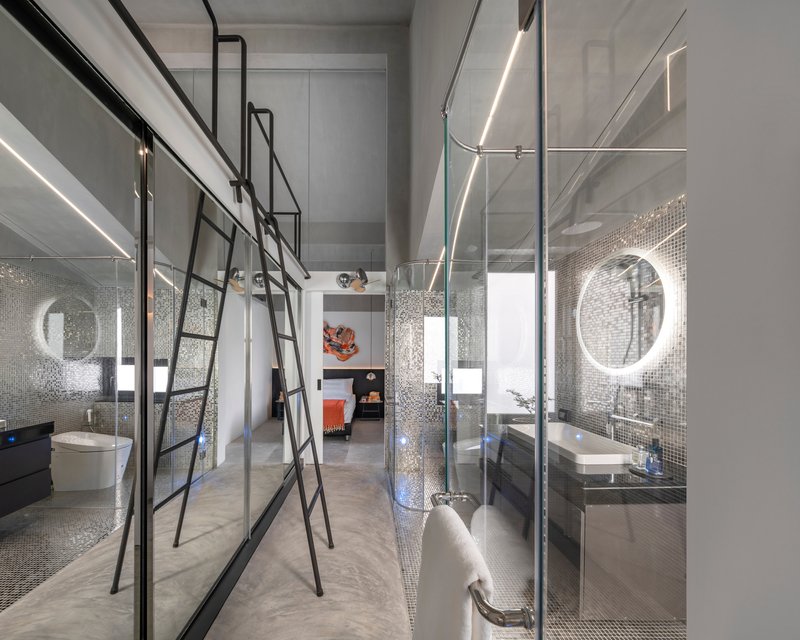 Bathroom interior with silver mosaic tile surfaces, glass partitions, steel ladder, and circular illuminated mirror