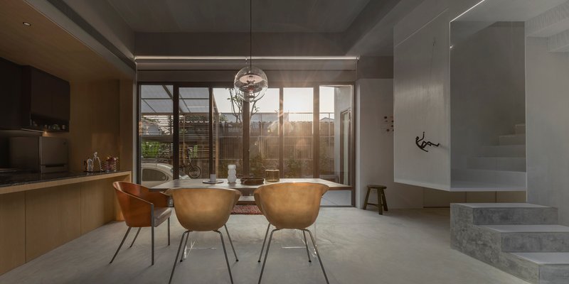 Dining table with copper-toned chairs facing sliding glass doors opening to a timber-screened courtyard at dusk