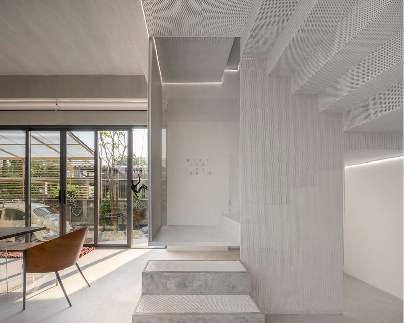 Perforated metal staircase with integrated lighting rising alongside a glazed courtyard view