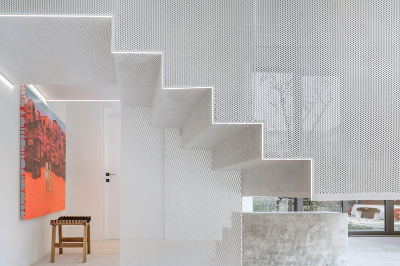 White perforated metal staircase wrapping around a concrete volume beneath integrated linear ceiling lighting