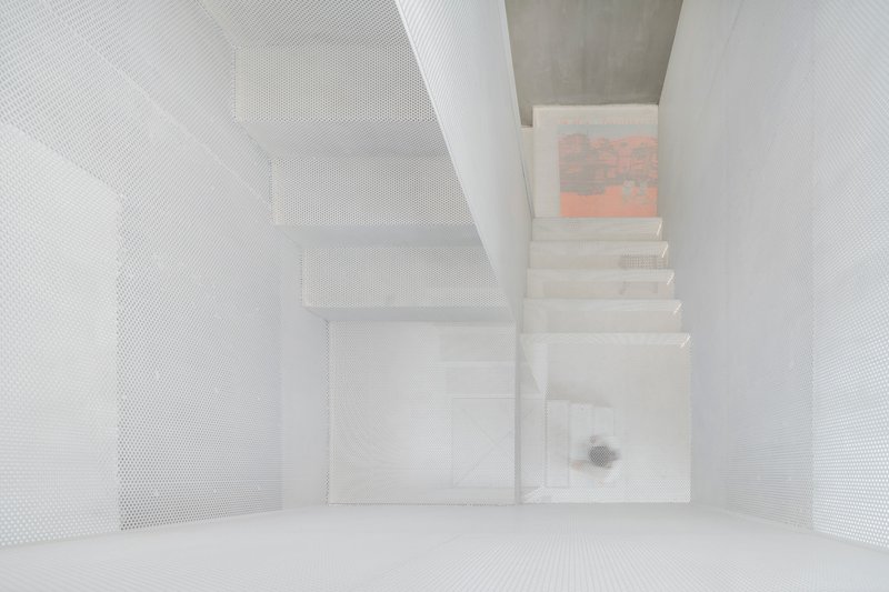 Top-down view of the white perforated metal stairwell with painting visible on upper landing