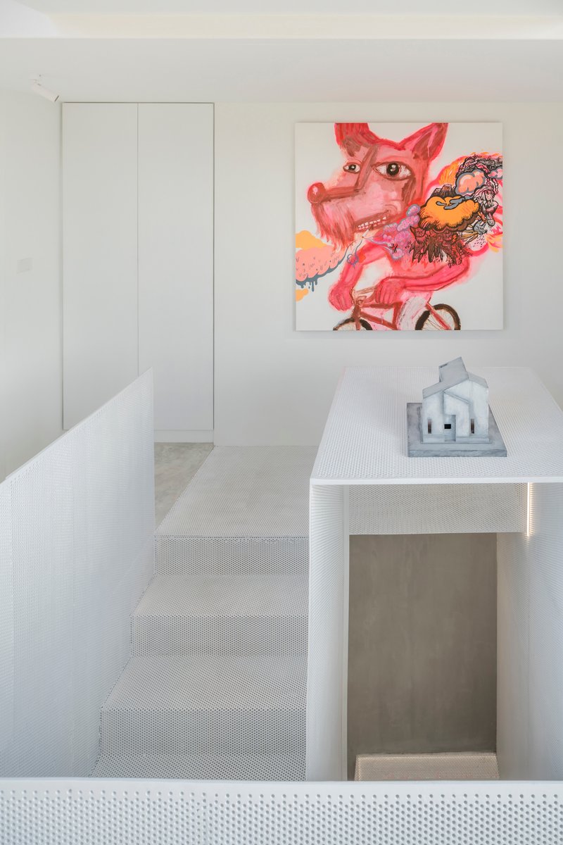 White perforated metal staircase rising past a tall storage cabinet and colorful artwork on the wall