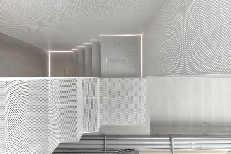Looking down through the perforated metal floor and stairwell with integrated linear lighting along the edges