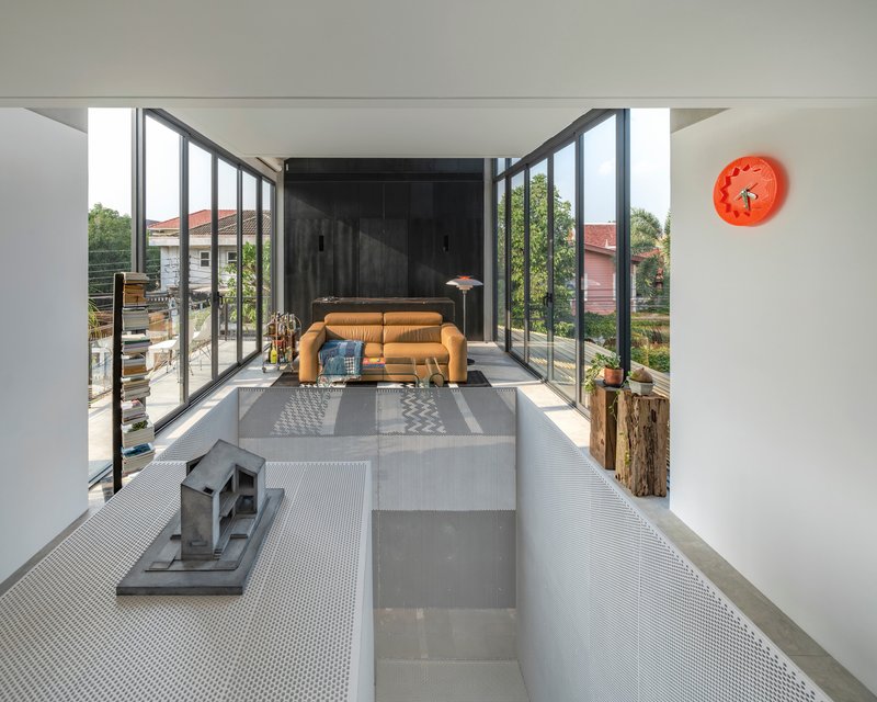Double-height living space with floor-to-ceiling steel glazing opening to a wooden deck and green treetops