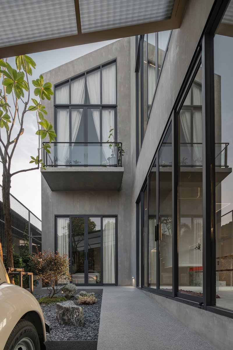 Concrete courtyard with gravel beds and planted trees framed by steel frame windows