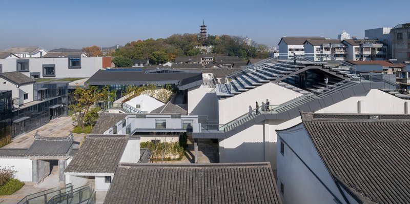 Aerial view of interconnected courtyards with white volumes and grey-tiled roofs among surrounding neighborhood buildings