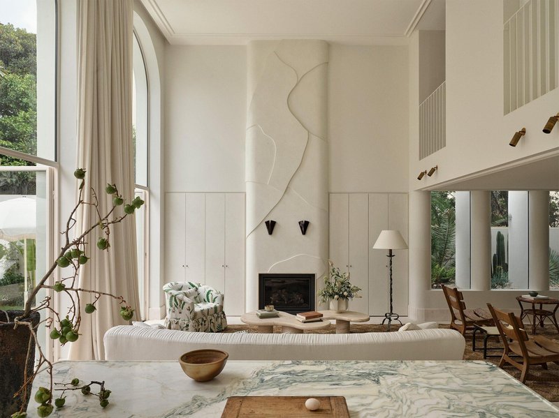 Double-height living room with arched windows, a fireplace, and a sculptural plaster relief above