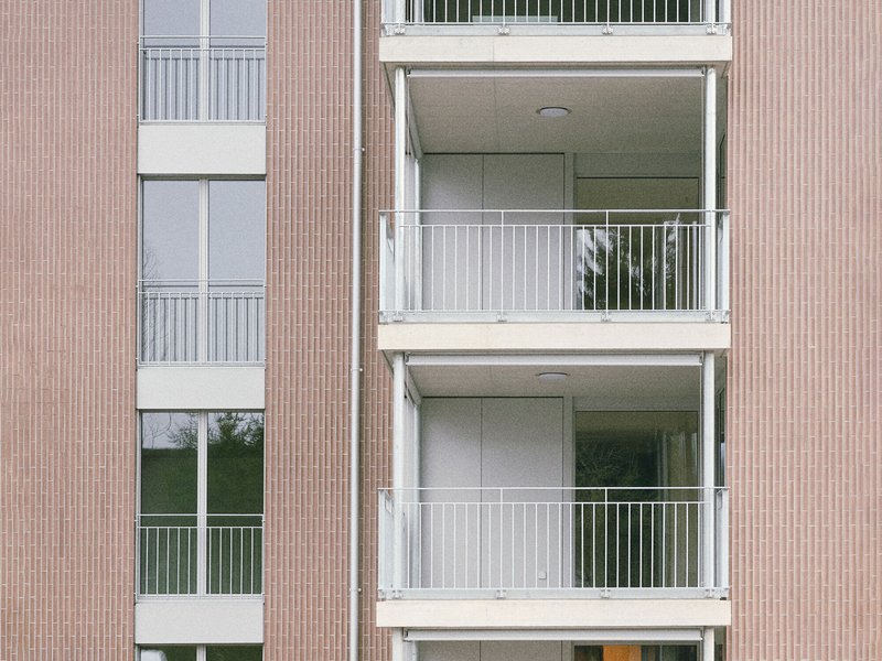 Close-up of stacked white balconies with metal railings against the textured facade panels