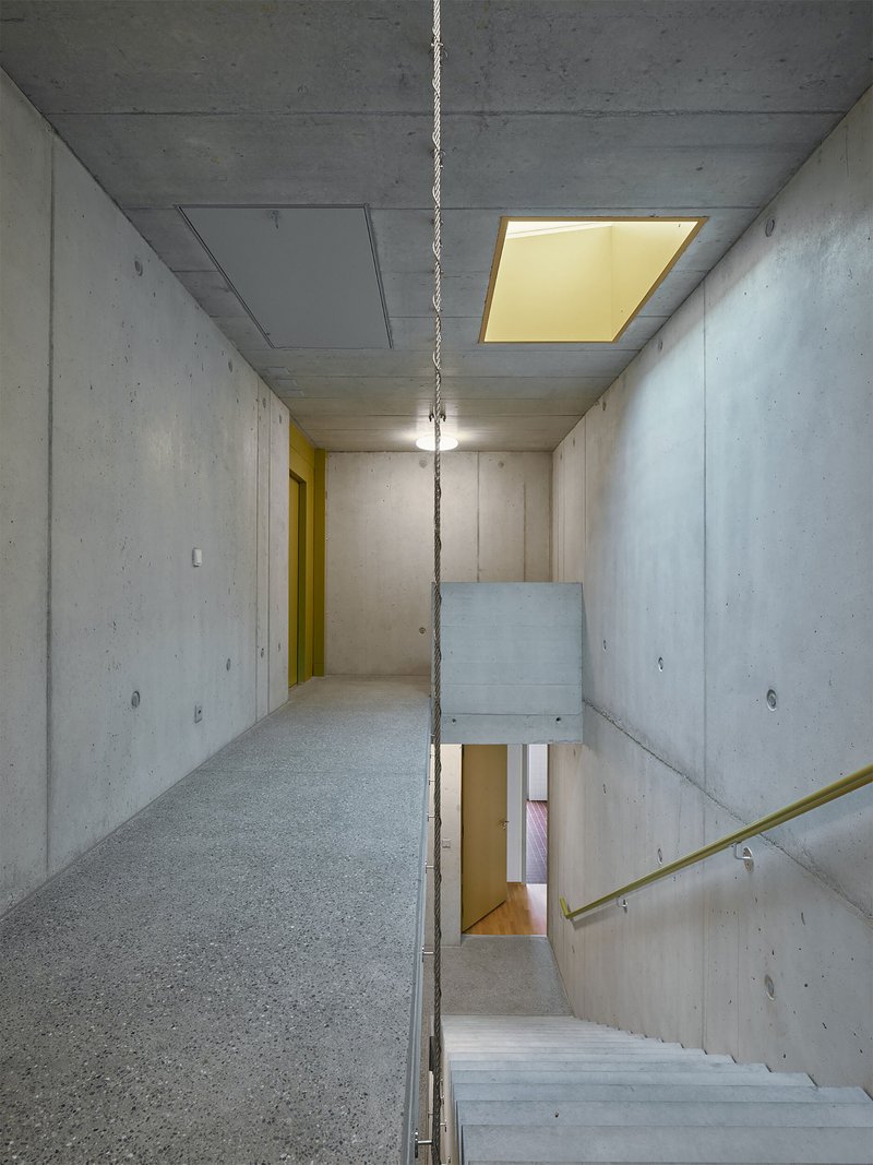 Concrete stairwell with exposed ceiling, brass handrail, and recessed skylight casting warm light