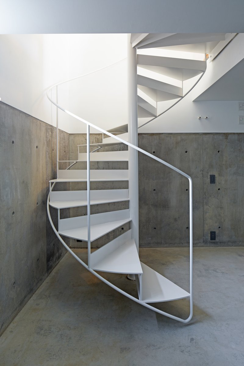 White metal spiral staircase against board-formed concrete walls with visible tie holes