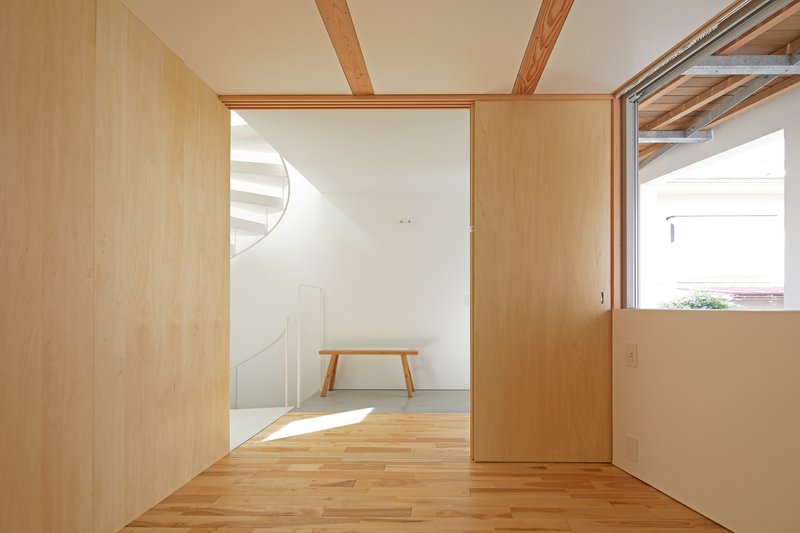 View through plywood-lined rooms with exposed timber beams and a wooden bench in sunlight