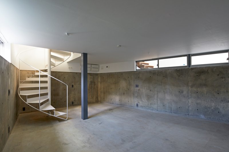 Lower level space with board-formed concrete walls, spiral stair, and steel column under clerestory windows