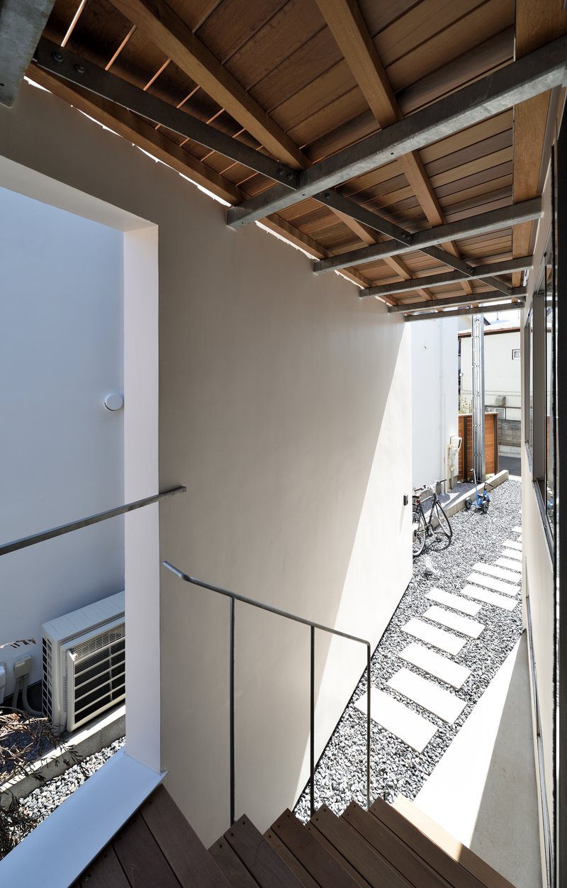 Exterior timber stair descending through gravel courtyard under slatted wood soffit with linear lighting