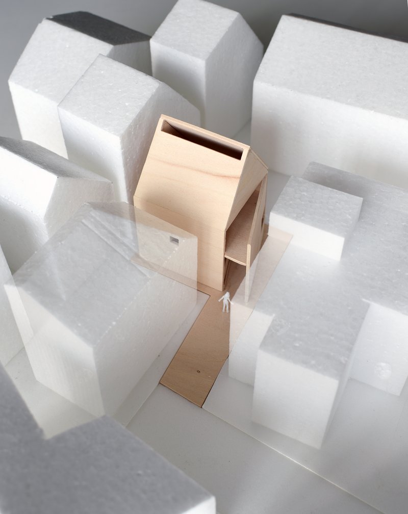 Physical model of a slender timber house form surrounded by white foam block massing