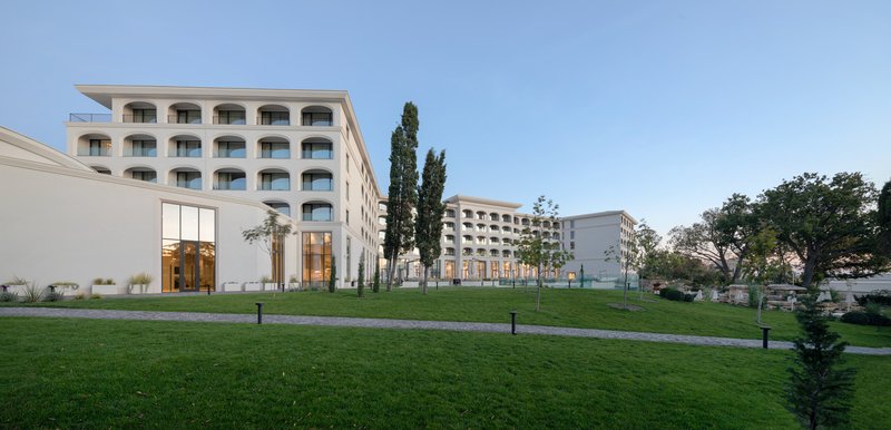 View across the lawn toward the arched facade and low glazed entry volume under blue sky