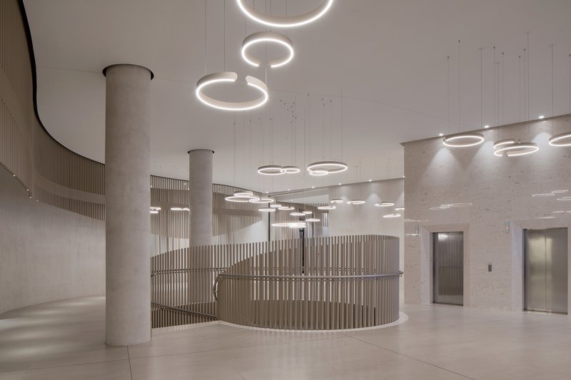 Reception area with curved slatted timber desk enclosure beneath cascading ring chandeliers and concrete columns