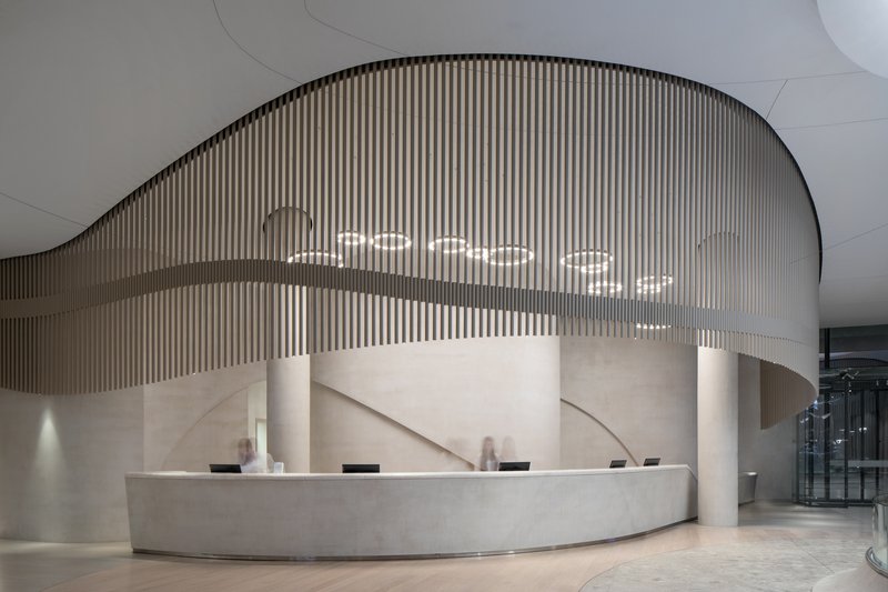 Reception desk with curved stone face under a flowing slatted screen and pendant lights
