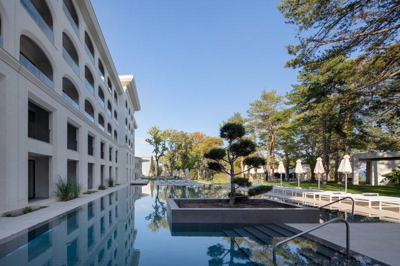 Reflecting pool running alongside the white facade with arched openings and planted courtyard