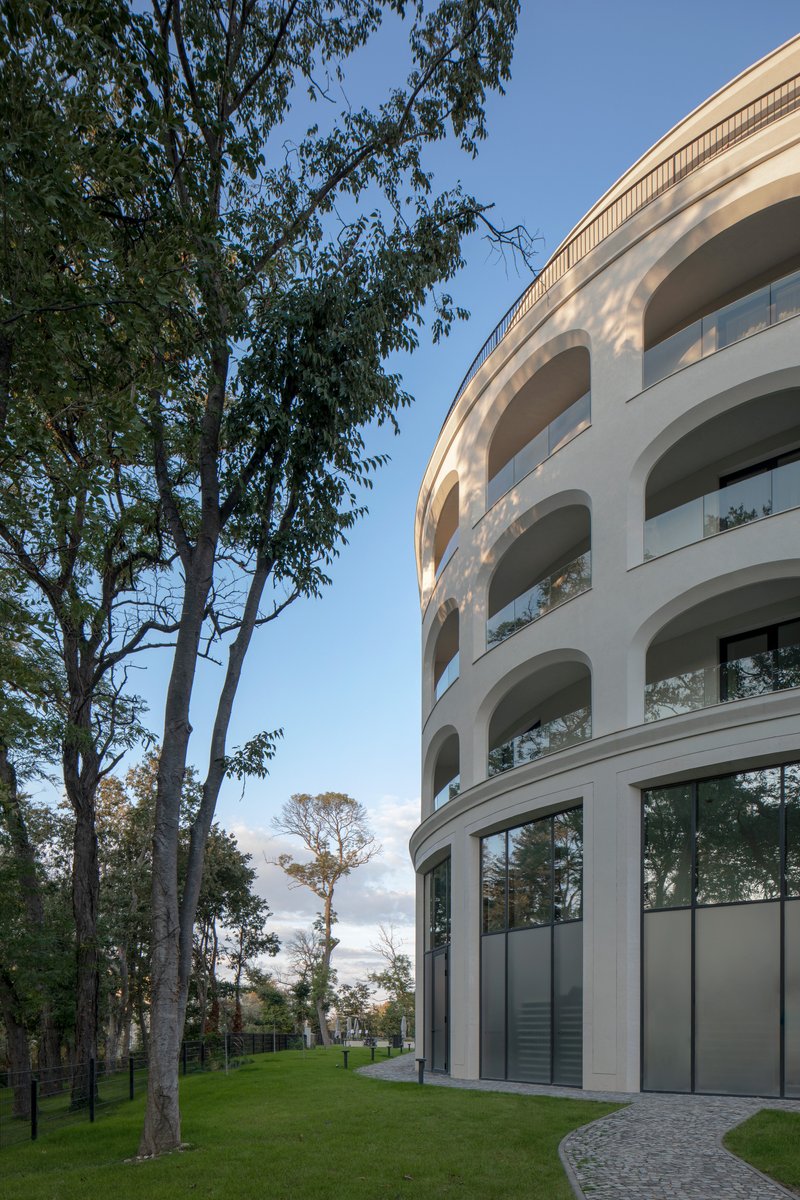 Curved corner of the white facade with stacked arched balconies beside mature trees