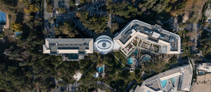 Drone view of the complex showing curved rooftops, circular courtyard and surrounding forest