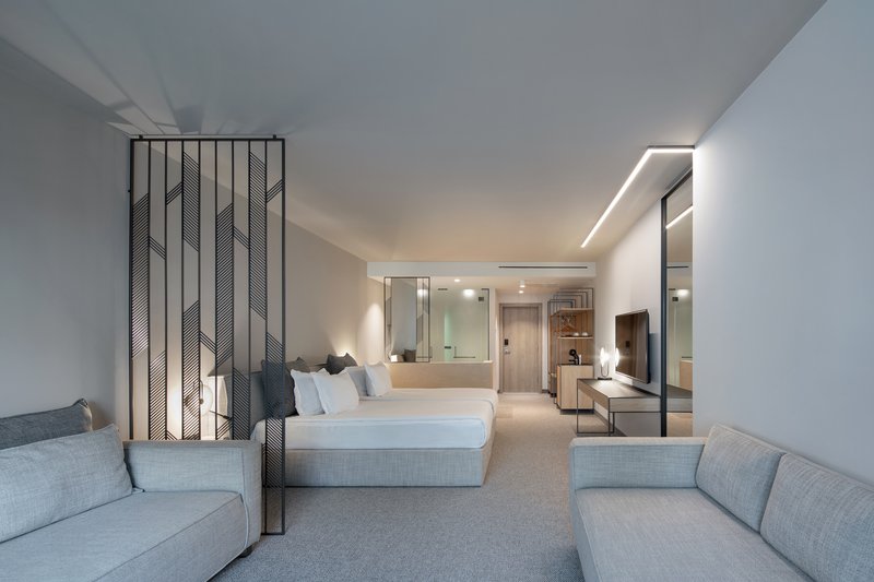 Guest suite with perforated metal room divider separating sleeping area from lounge under recessed ceiling lighting