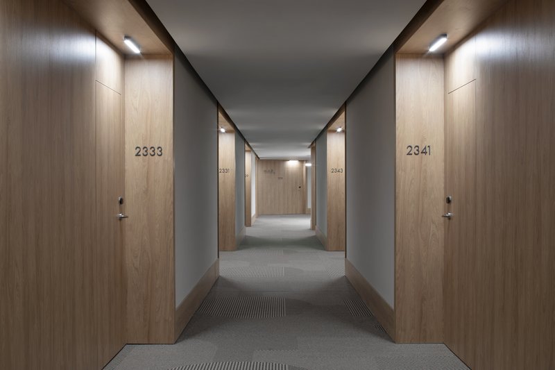 Hotel corridor with numbered wood doors and grey walls under recessed linear lighting