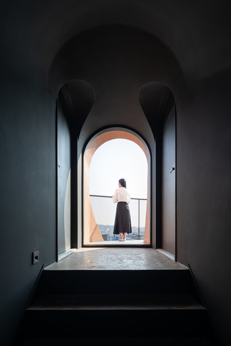 Dark arched corridor with a person standing at the illuminated opening overlooking the cityscape