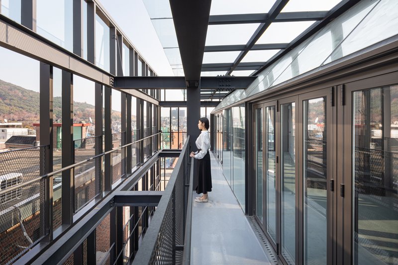 Exterior walkway with perforated metal balustrade and black steel overhead beams at dusk