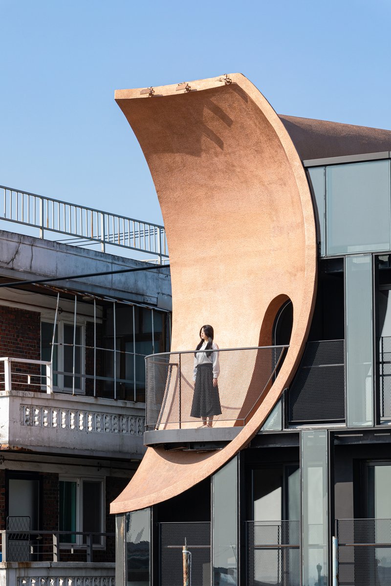 Curved timber balcony cantilevering from the facade with a figure standing in afternoon light