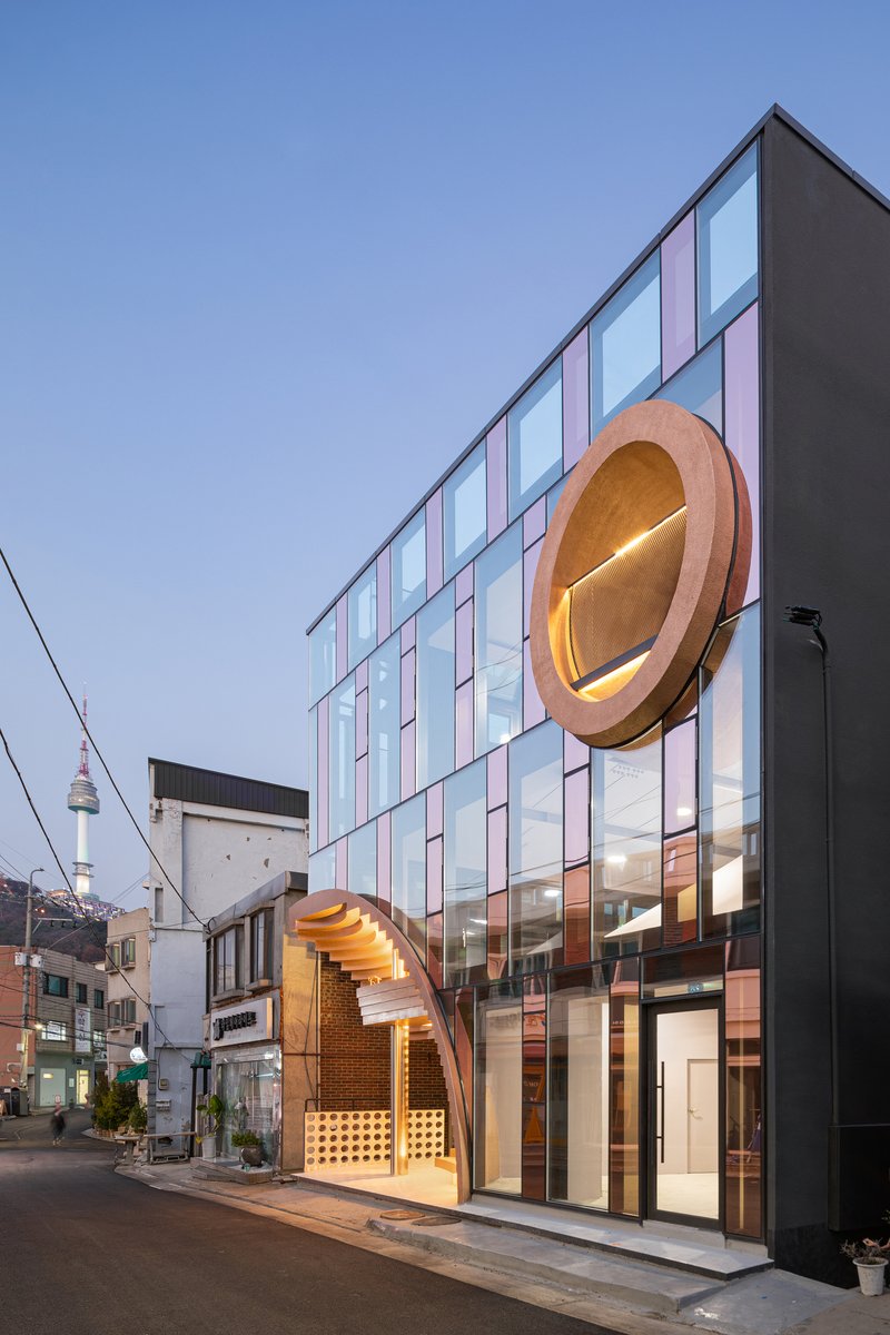 Evening view of the glass facade and circular timber porthole element illuminated from within at dusk