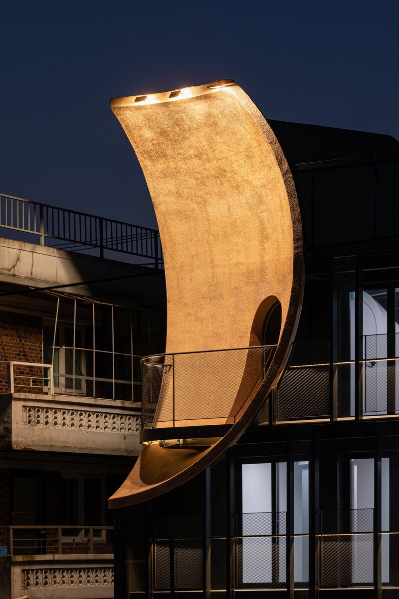 Night view of the illuminated curved timber element cantilevering from the building volume