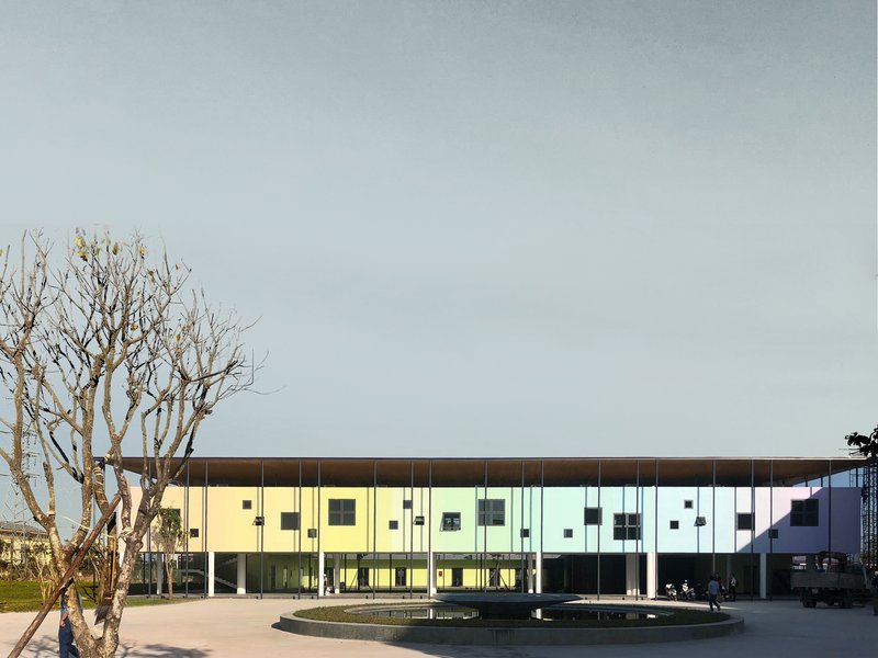 Front elevation showing the pastel-paneled facade with cantilevered overhang and bare tree beside a circular fountain