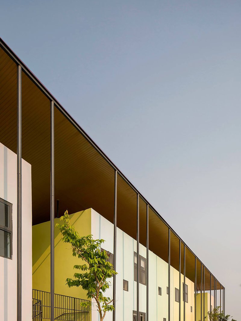 Long sloped roof with wood soffit extending over white facade volumes and a planted courtyard at dusk