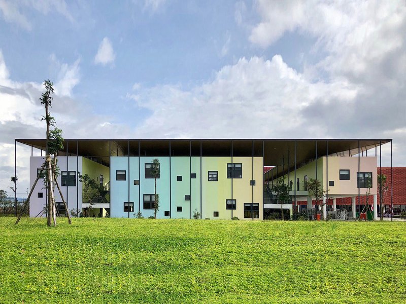 Long view of the pastel-colored facade with scattered square windows above a lawn under scattered clouds