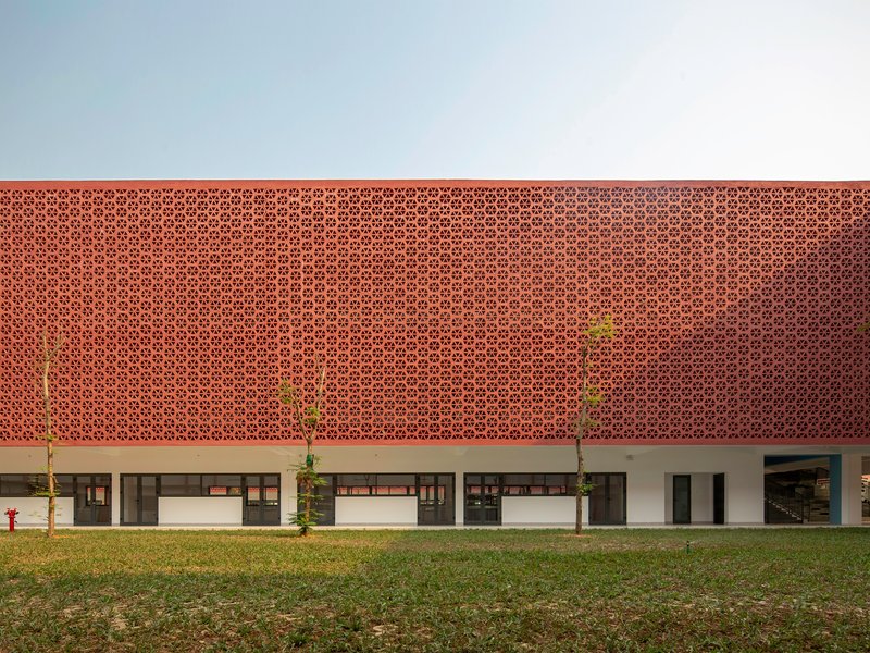 Two-story facade with perforated terracotta screen above white columns and planted saplings on grass lawn