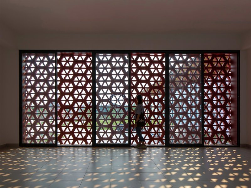 Interior corridor with triangular patterned screen wall casting dappled sunlight on polished floor