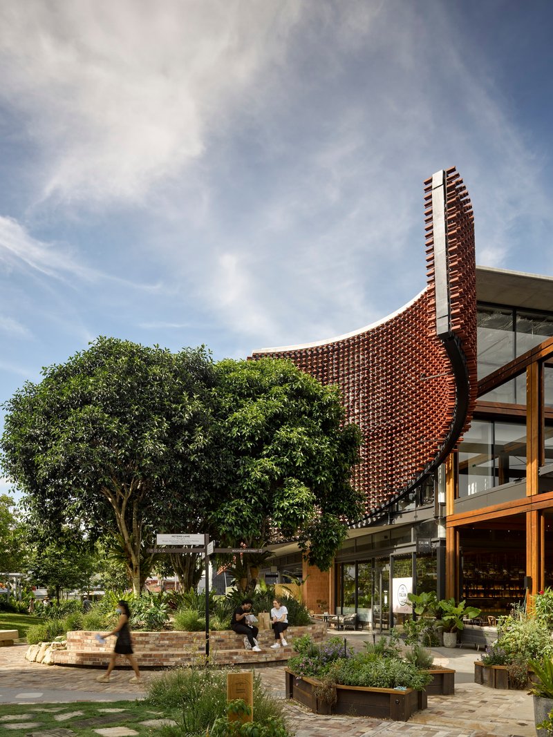 Curved perforated brick screen rising above glazed ground floor and landscaped courtyard with mature trees
