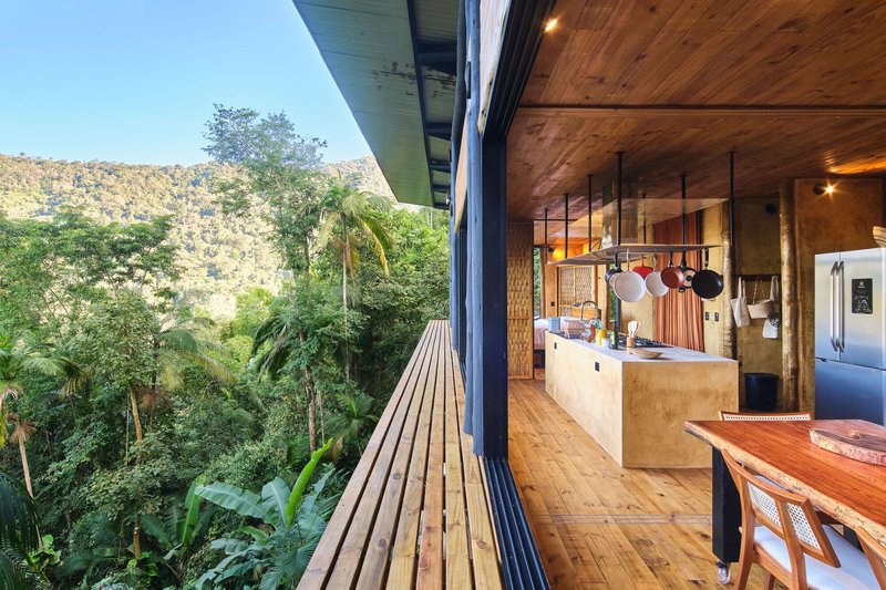 Open-plan kitchen and dining space with timber ceiling and slatted exterior deck overlooking forest
